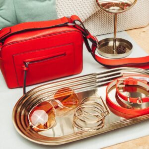 Stylish red handbag with matching accessories on a tray, perfect for a chic fashion statement.