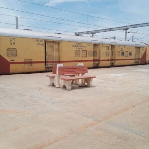 A deserted train station platform with a parked passenger train on a sunny day.