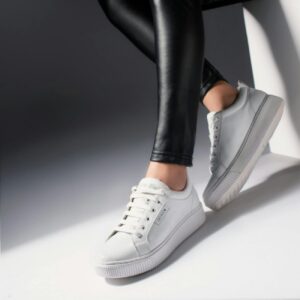 Close-up of woman's legs wearing trendy white sneakers and black leggings in studio lighting.