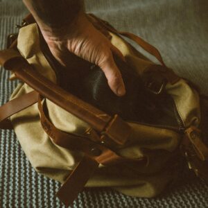 From above of crop anonymous male traveler putting photo camera into handbag while packing baggage before trip